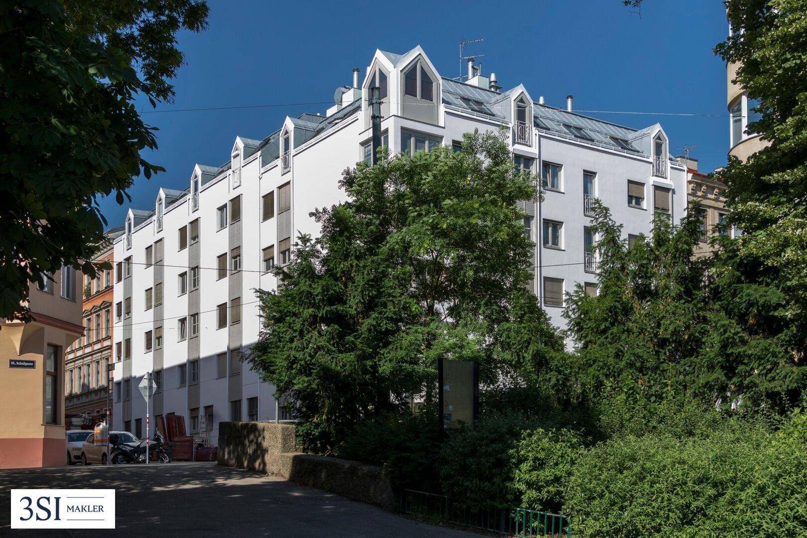Modernes Mehrfamilienhaus mit weißer Fassade, vielen Fenstern und markanten Dachgauben in urbaner Umgebung.