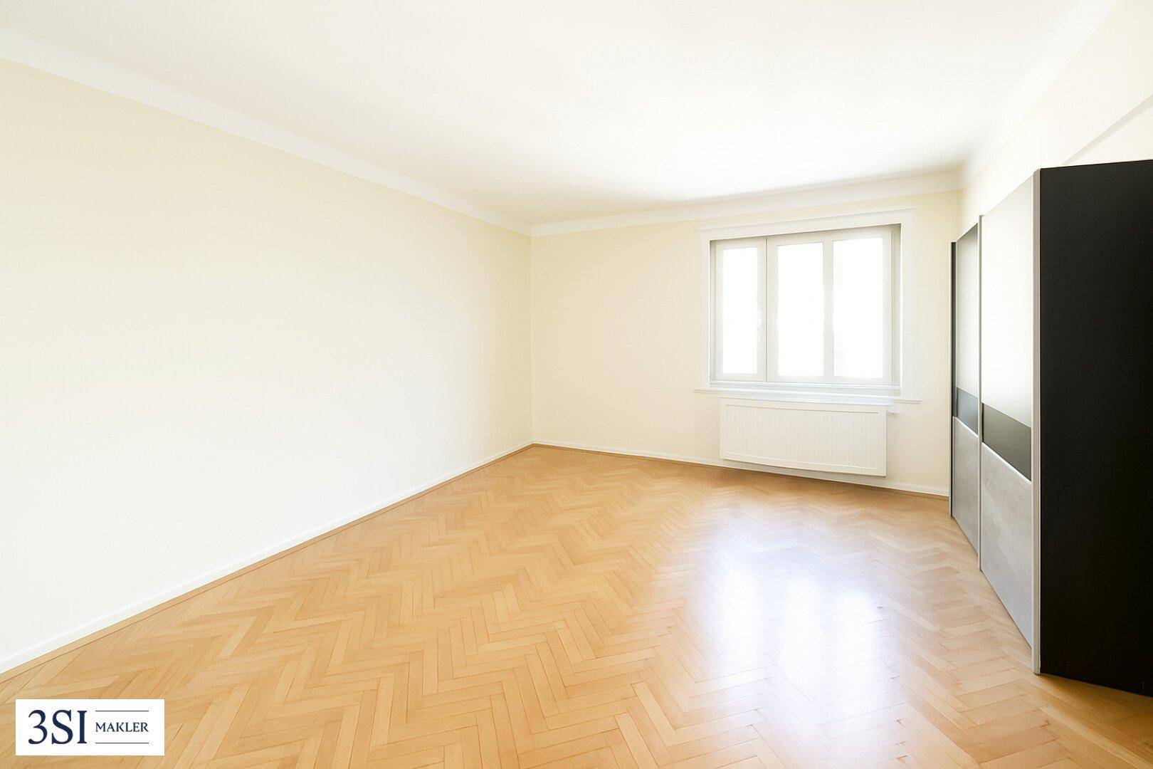 Geräumiger, unmöblierter Raum mit Fischgrätparkett und einem großen Fenster, ideal zur individuellen Gestaltung.