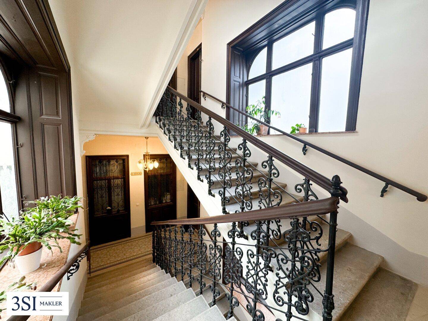 Prächtiges Treppenhaus mit schmiedeeisernem Geländer, Holzhandläufen und großen Fenstern.