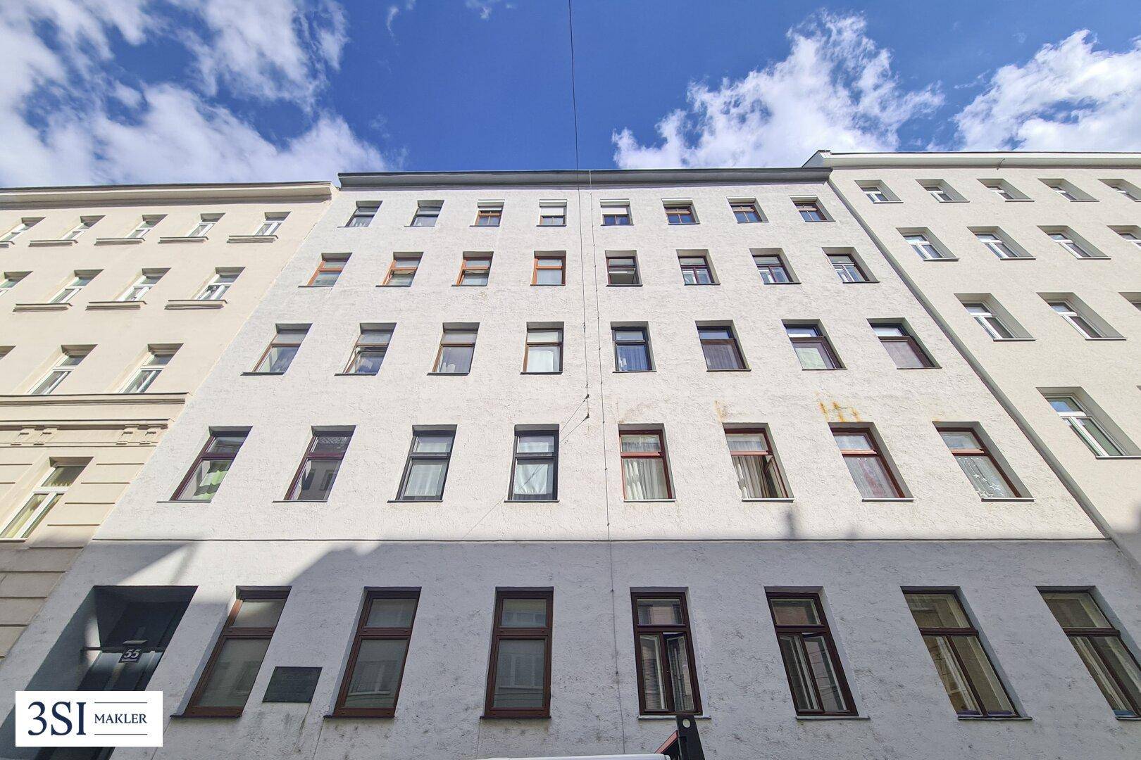 Die Fassade eines Mehrfamilienhauses mit vielen Fenstern unter blauem Himmel.