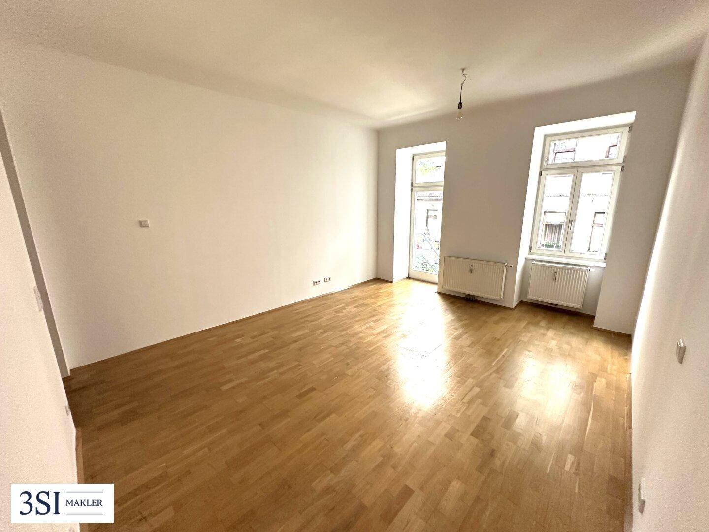 Leeres Zimmer mit hellen Wänden, Holzboden und großen Fenstern, ideal für vielfältige Nutzung.