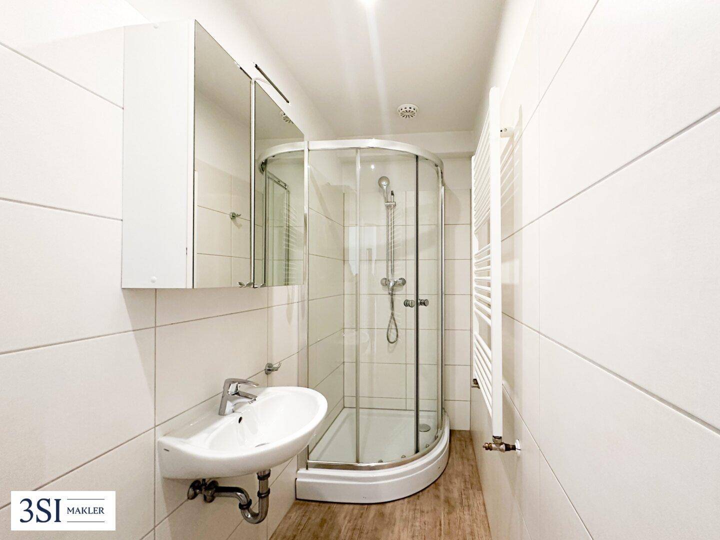 Helles Badezimmer mit Eckduschkabine, Einzelwaschbecken, Spiegelschrank und beheiztem Handtuchhalter.