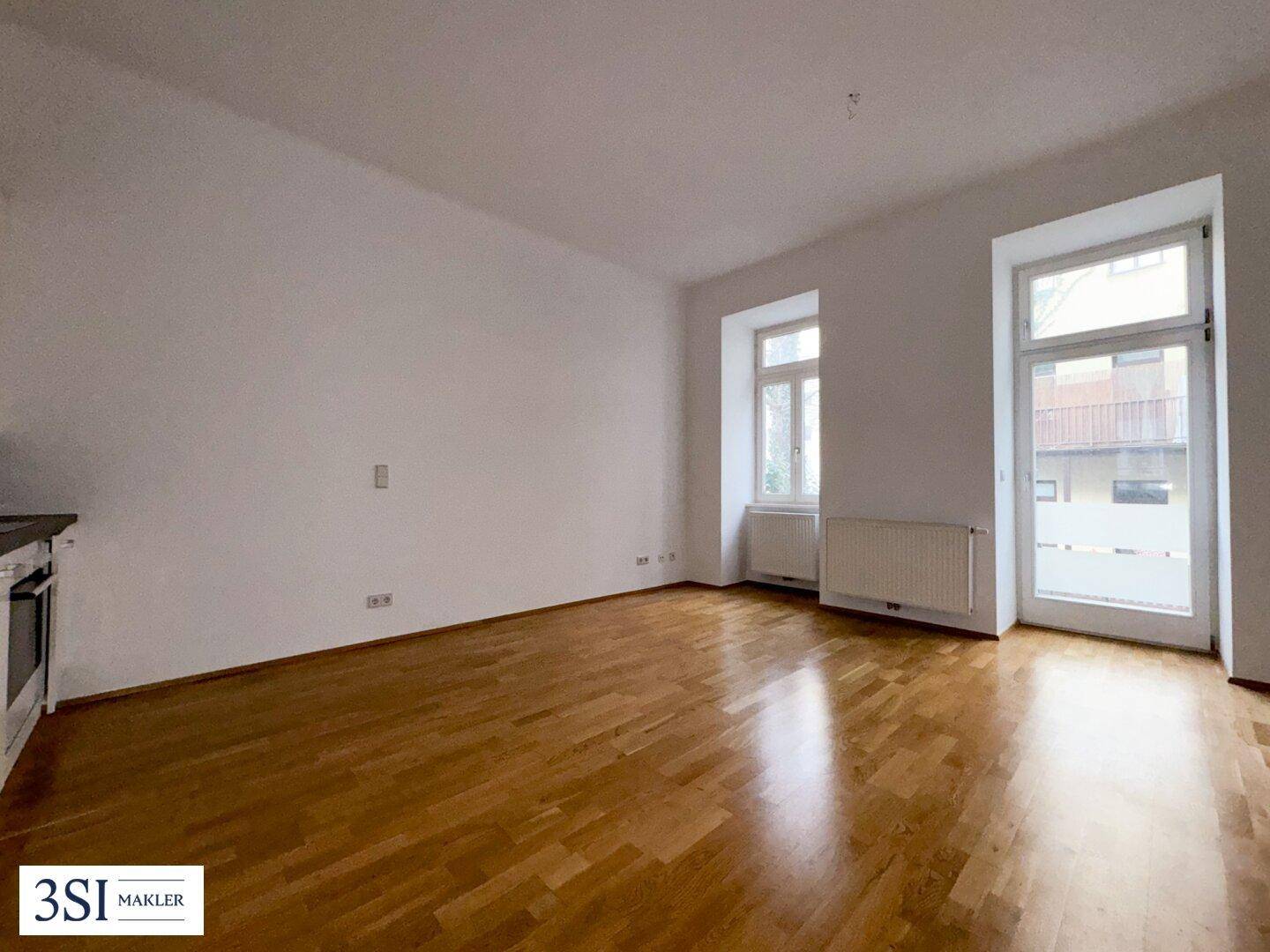 Helles Zimmer mit Holzboden, großen Fenstern und Heizkörpern, ideal als offener Wohnbereich.