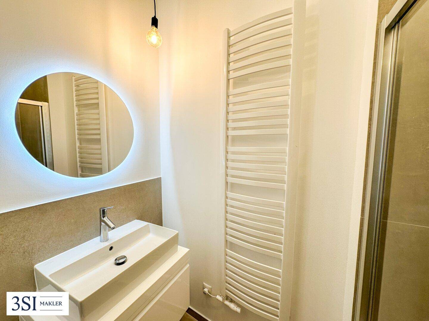 Modernes Badezimmer mit beleuchtetem Spiegel, Einzelwaschbecken und Handtuchheizkörper.