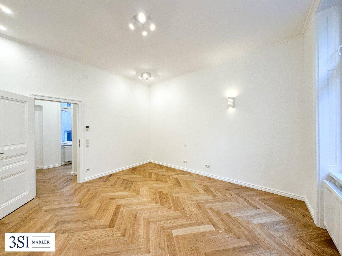 Leerer Raum mit elegantem Fischgrätparkett und weiß gestrichenen Wänden.