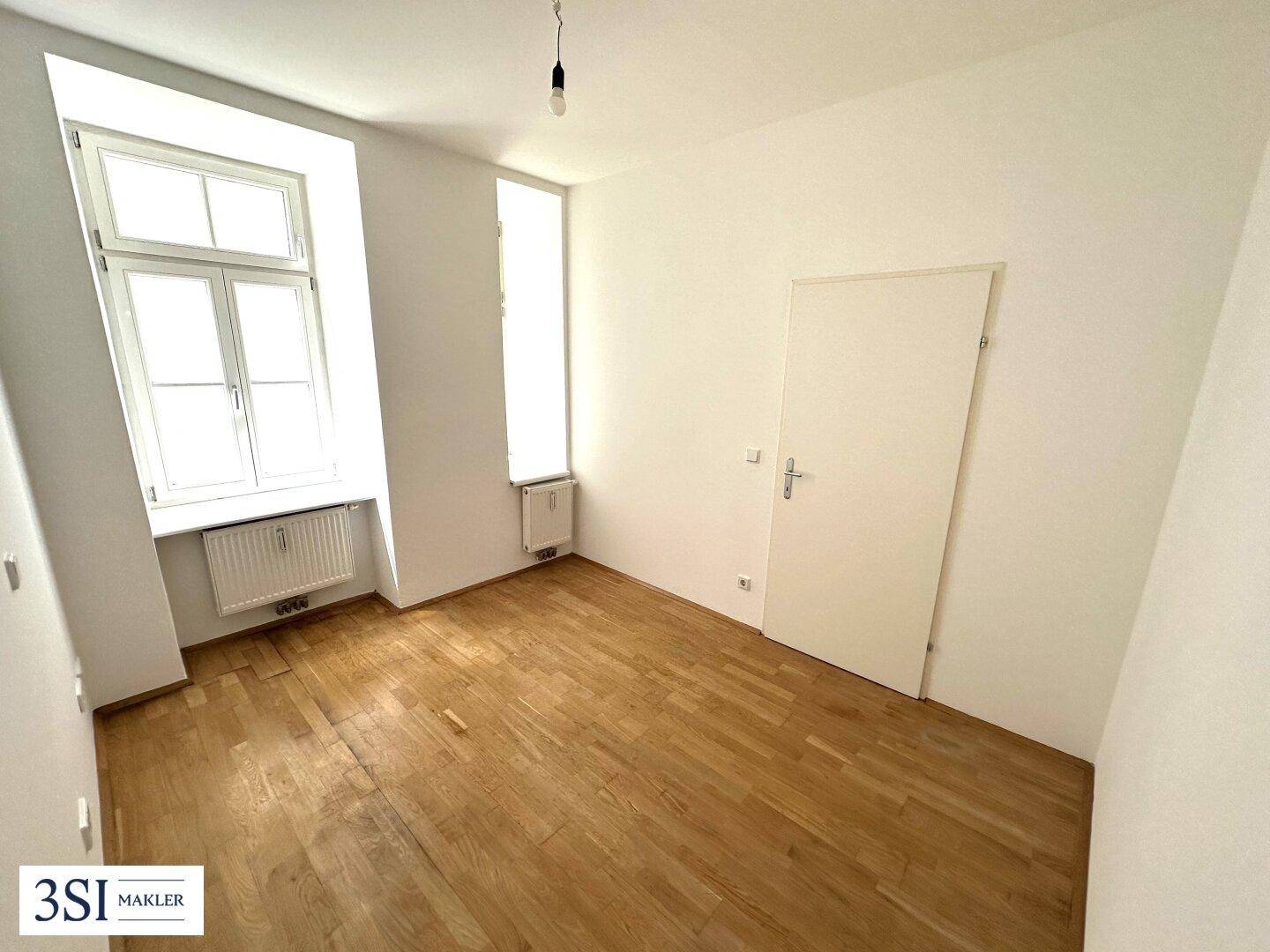 Unmöbliertes Schlafzimmer mit Holzboden und großen Fenstern, bereit für persönliche Einrichtung.