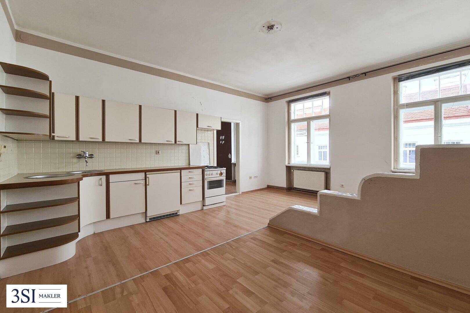 Geräumige, leere Wohnküche mit Einbauküche und Holzboden, bereit zur Gestaltung.