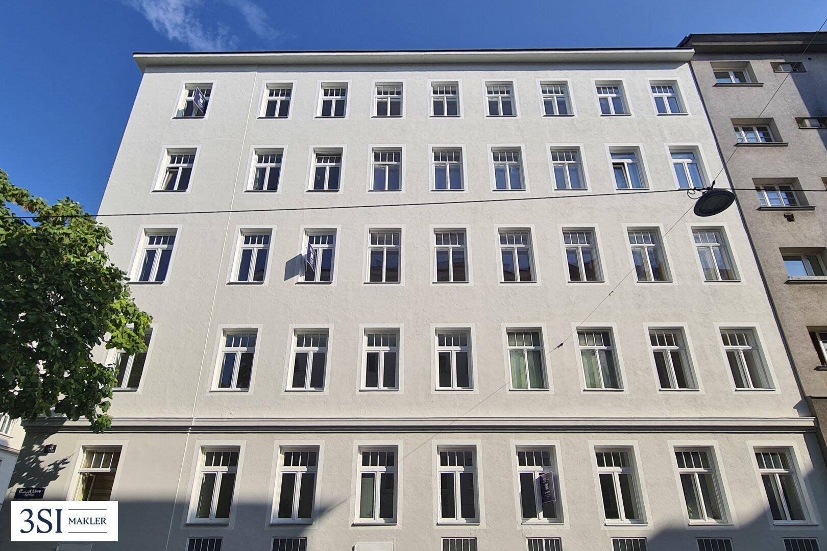 Die moderne Fassade eines Mehrfamilienhauses mit vielen Fenstern unter blauem Himmel.