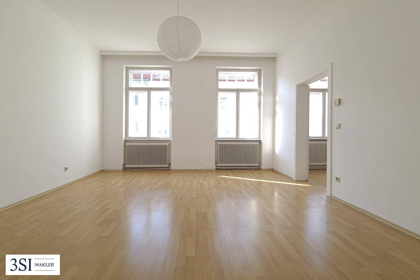 Geräumiges, leeres Zimmer mit Parkettboden, hohen Decken und zwei großen Fenstern.