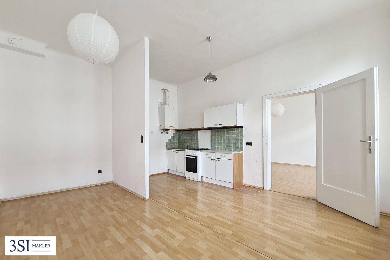 Heller Raum mit Kochnische, Parkettboden und Zugang zu einem weiteren Zimmer.