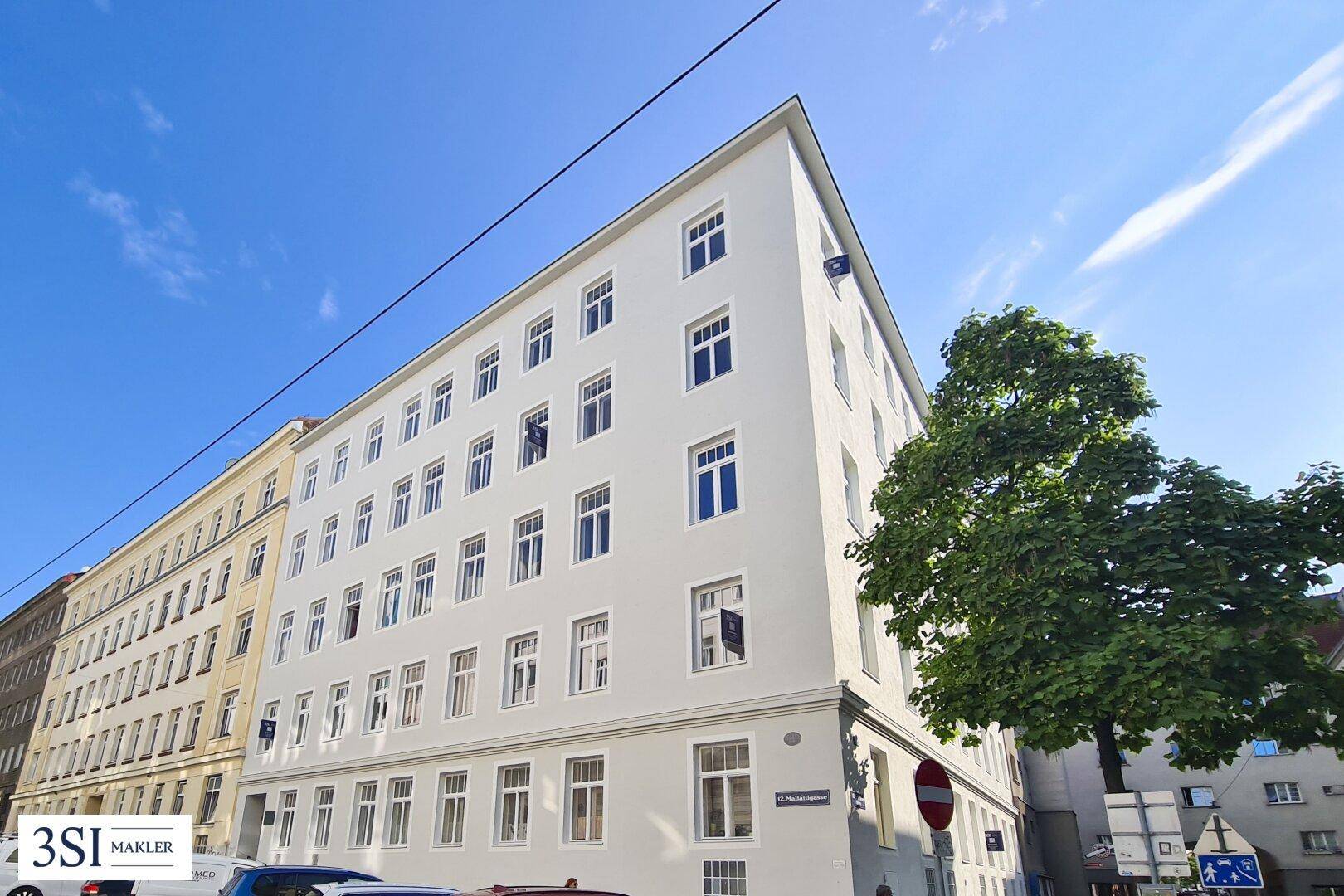Eckansicht eines gepflegten Mehrfamilienhauses mit vielen Fenstern und einem Baum.