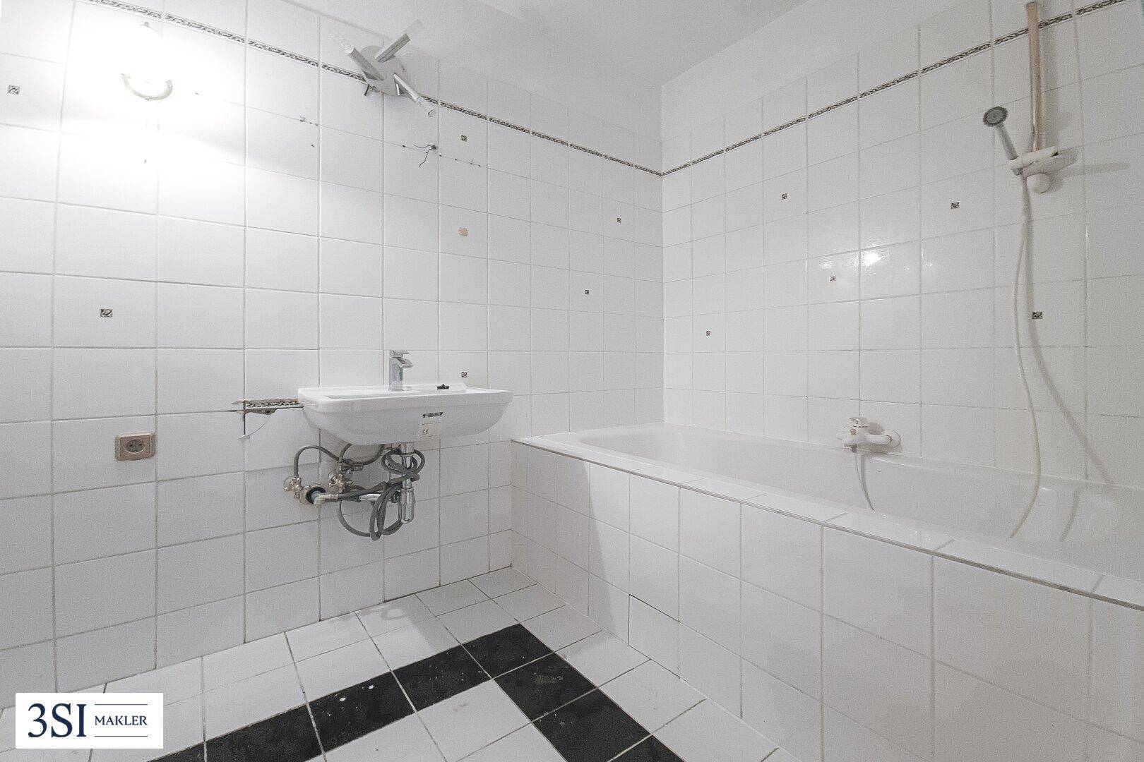 Einfaches Badezimmer mit weißen Fliesen, Badewanne und Waschbecken, das eine Renovierung benötigt.