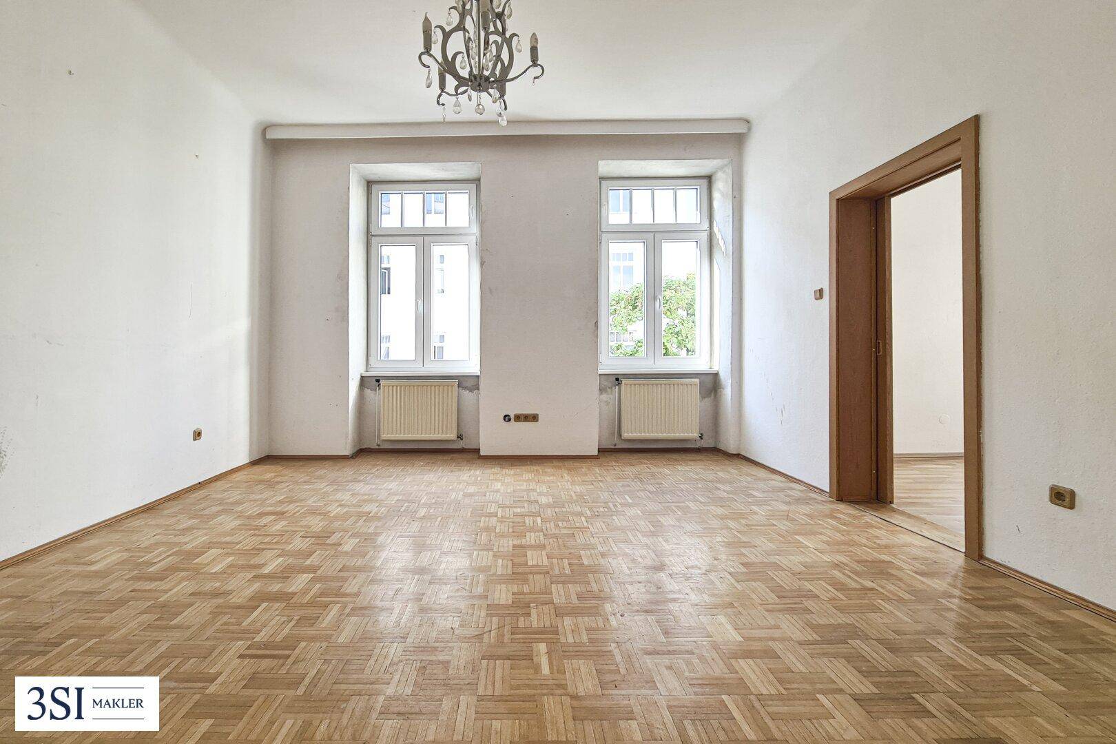 Geräumiges, unmöbliertes Wohnzimmer mit Fischgrätparkett und hohen Fenstern, bereit zur individuellen Gestaltung.