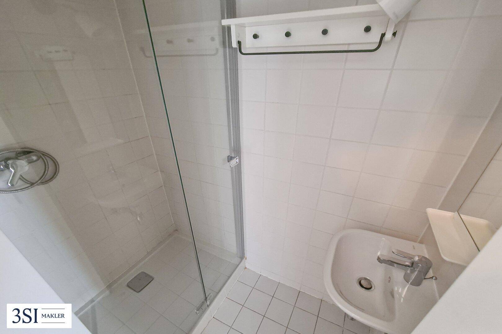 Kleines Badezimmer mit weiß gefliesten Wänden, Dusche und Waschbecken.