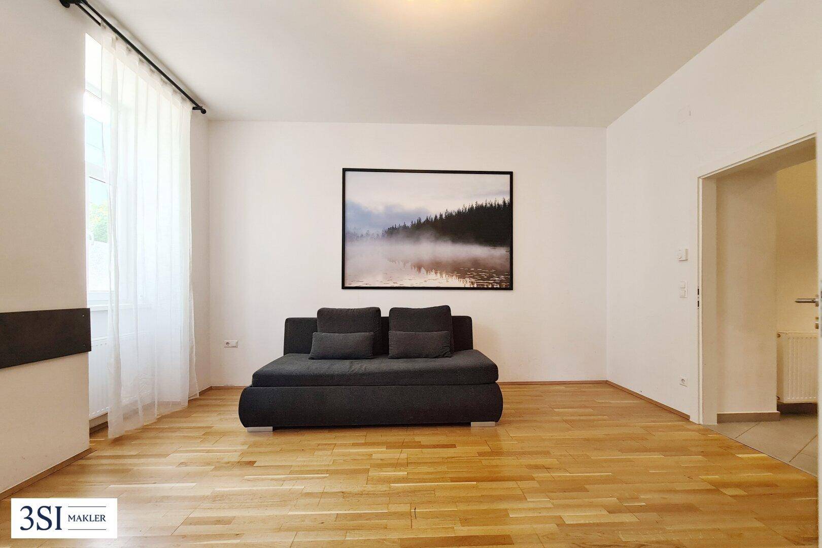 Helles Wohnzimmer mit bequemer Couch, Holzboden und einem großen Wandbild.