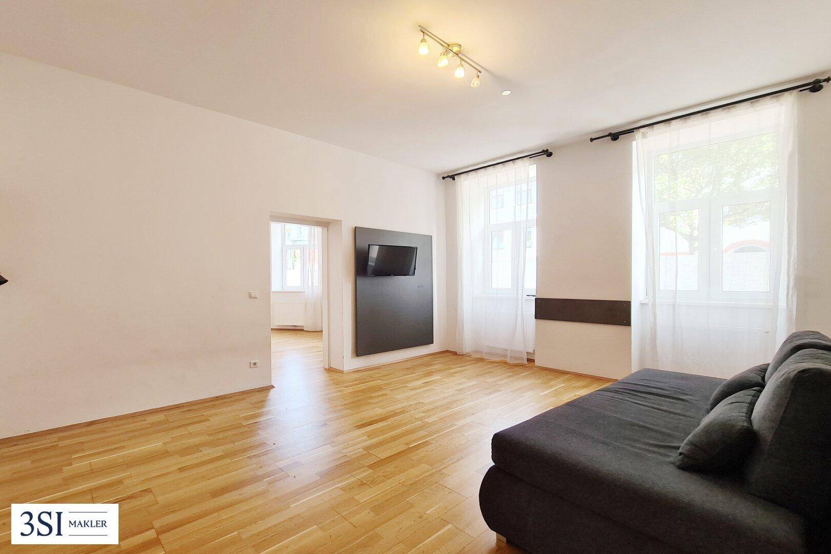 Geräumiges Wohnzimmer mit hellem Holzboden und Zugang zu einem weiteren Raum.
