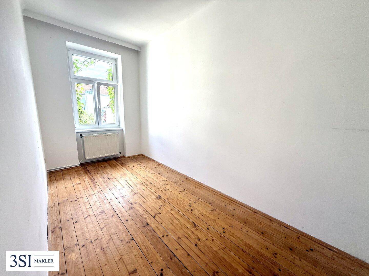 Heller, leerer Raum mit Holzdielenboden und einem großen Fenster.