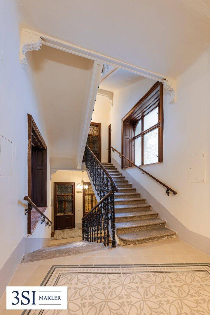 Elegantes Treppenhaus mit Steinstufen, schmiedeeisernem Geländer und hohen Decken.