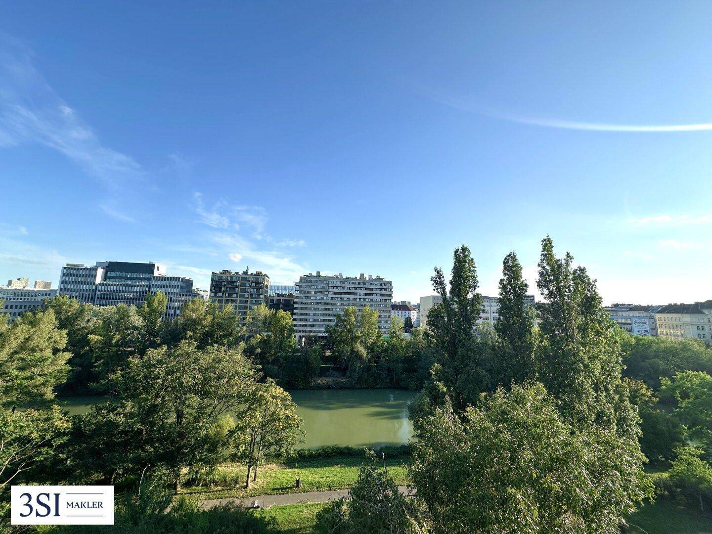 Weitläufiger Blick über einen See und eine grüne Parklandschaft mit städtischer Skyline im Hintergrund.