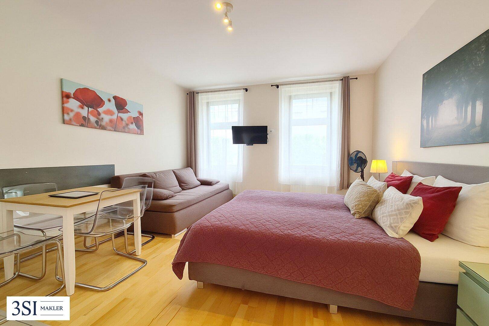 Helles Schlafzimmer mit Doppelbett, Schlafsofa und Esstisch auf Holzboden.