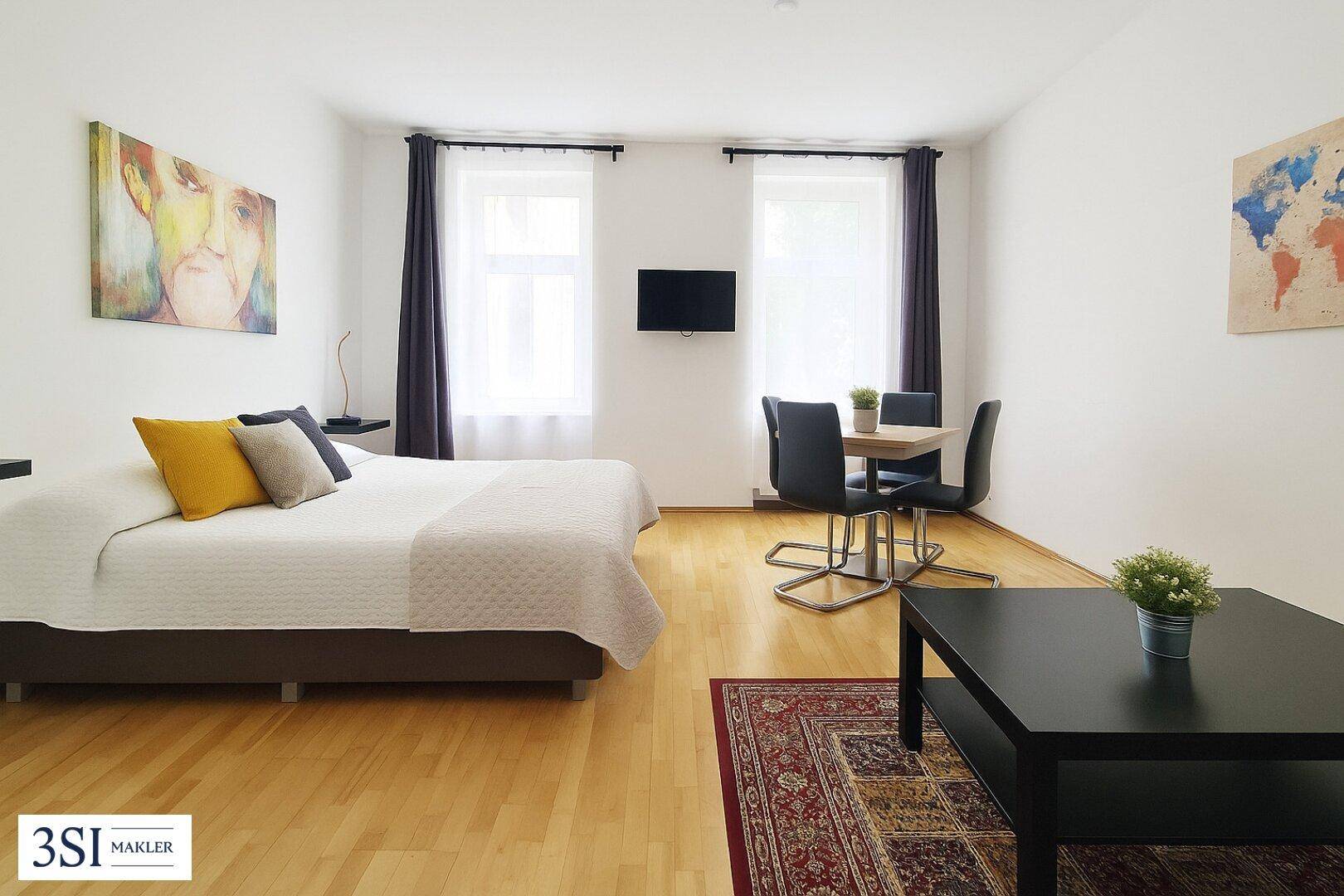 Gemütliches Schlafzimmer mit Doppelbett, Esstisch und Holzboden in heller Atmosphäre.