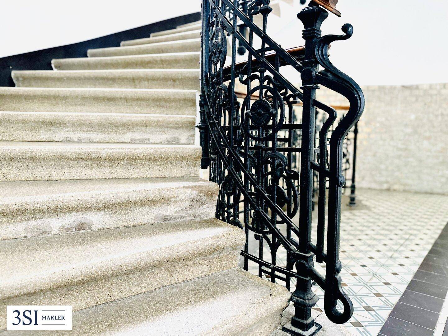 Elegante Steintreppe mit kunstvollem schmiedeeisernem Geländer in einem historischen Treppenhaus.