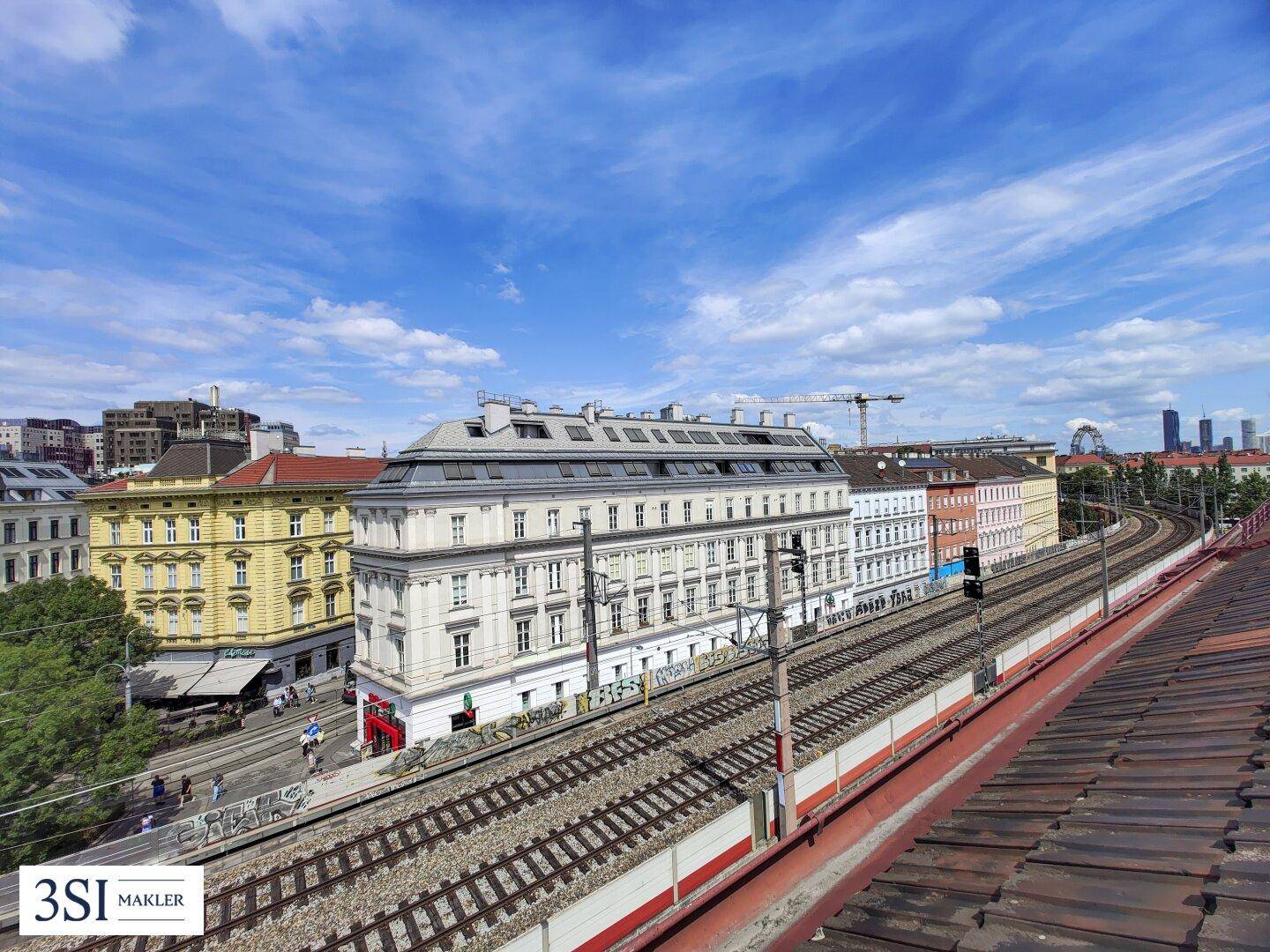 Panoramablick über die Stadt mit Bahngleisen und Dächern im Vordergrund unter weitem Himmel.