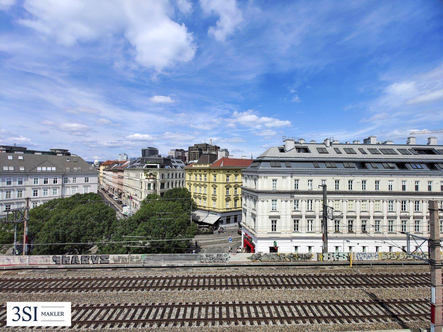 Weitläufiger Stadtblick über Bahngleise und historische Gebäude unter blauem Himmel.