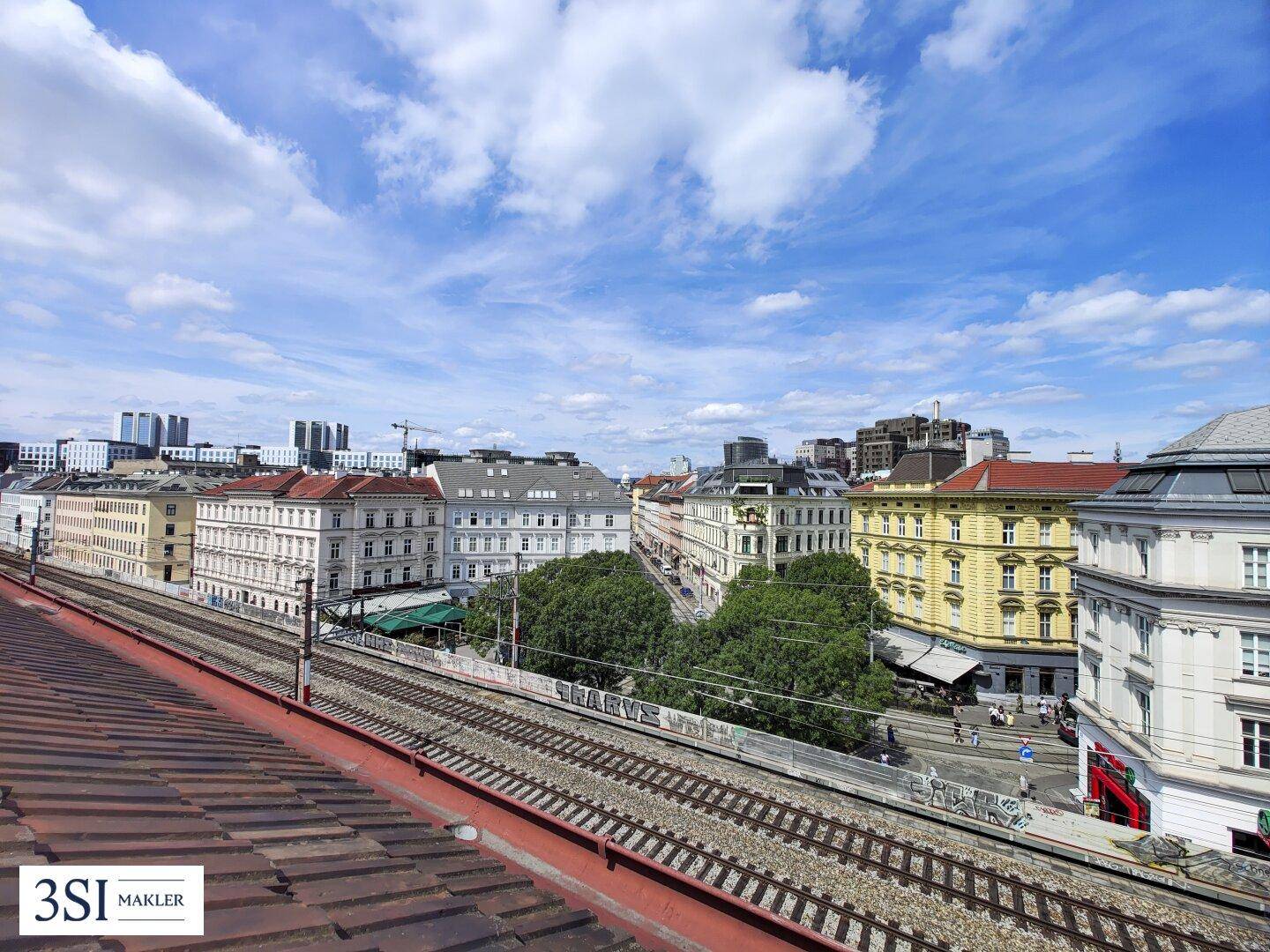 Weitläufiger Stadtblick mit Bahngleisen und urbaner Architektur unter blauem Himmel.
