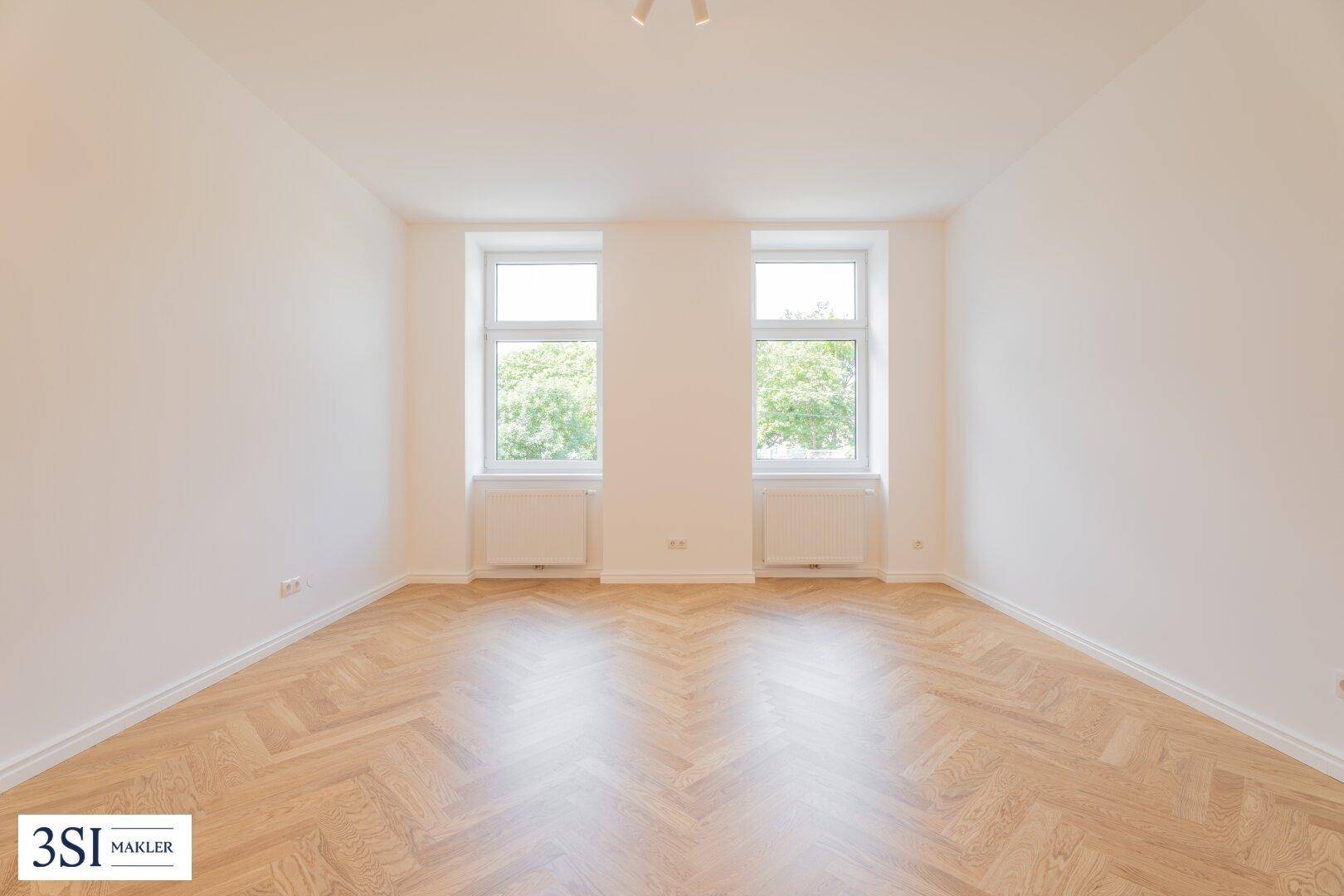 Helles und geräumiges Zimmer mit Fischgrätparkett und zwei Fenstern, bereit zur individuellen Gestaltung.