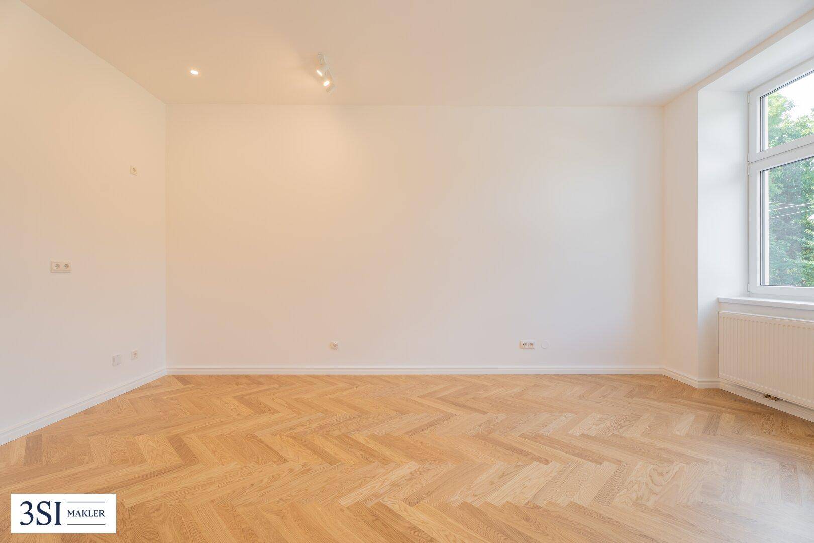 Lichtdurchfluteter Raum mit elegantem Fischgrätparkett und einem großen Fenster, ideal für individuelle Gestaltung.