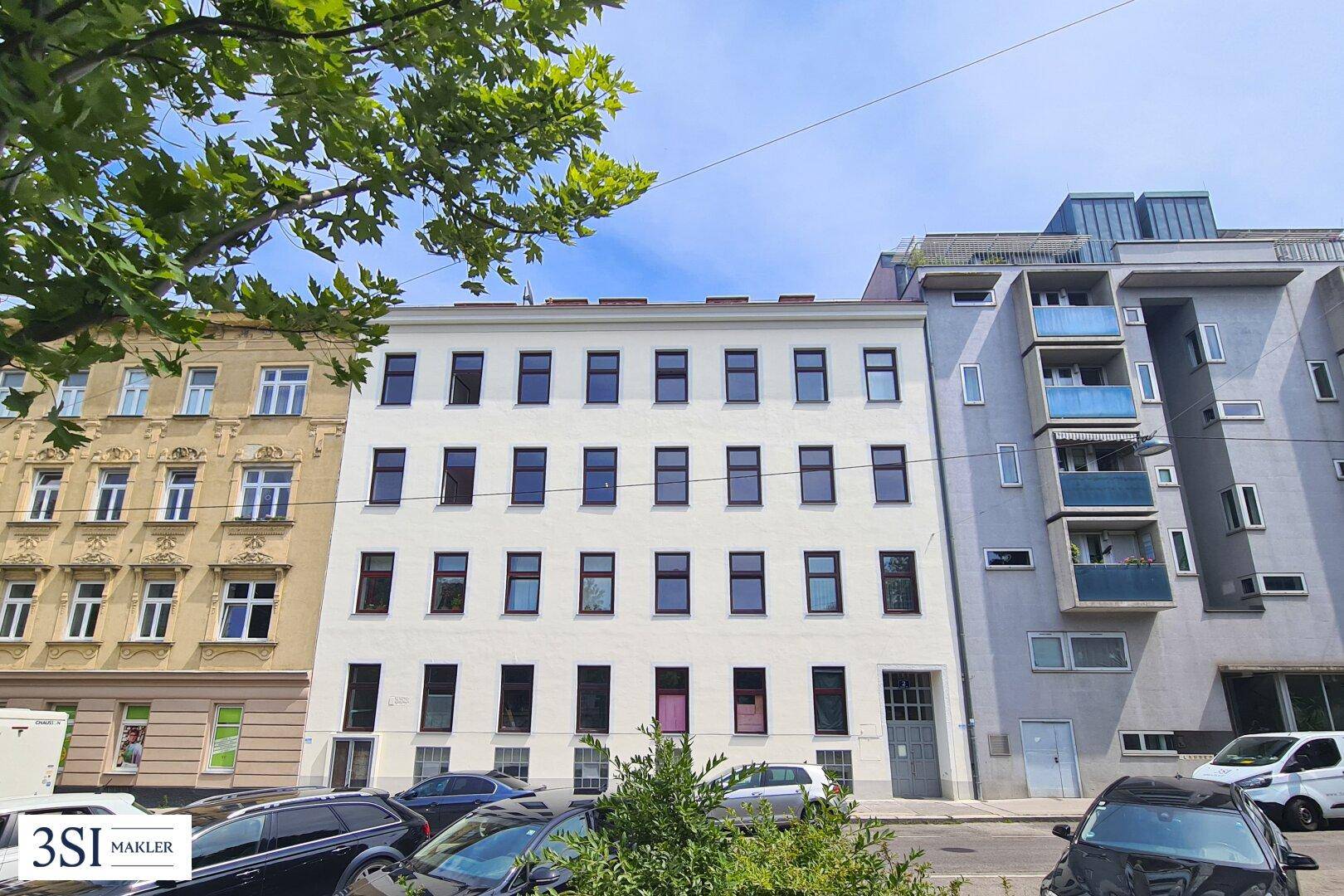 Klassische Fassade eines Mehrfamilienhauses in städtischer Umgebung mit parkenden Autos.