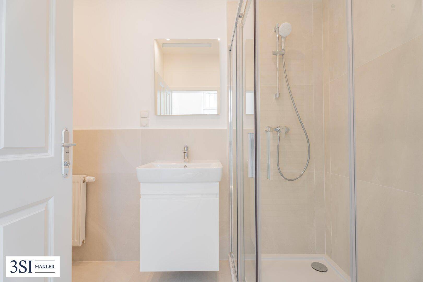 Modernes Badezimmer mit Duschkabine, Waschbecken und hellen Fliesen in neutralen Farbtönen.
