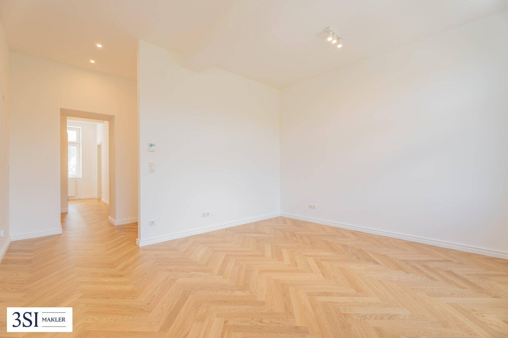 Heller Raum mit Fischgrätparkett und offenem Zugang zu einem weiteren Zimmer.