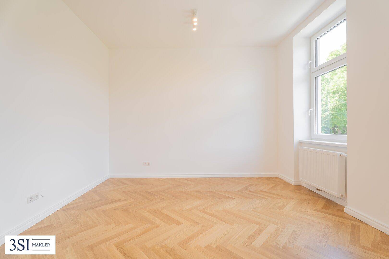 Geräumiges Zimmer mit Fischgrätparkett und einem großen Fenster für viel Tageslicht.