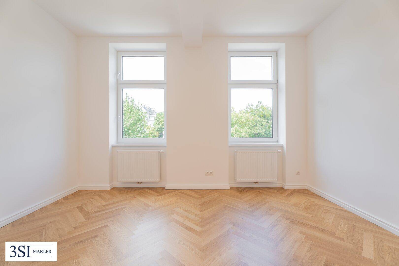 Geräumiges Zimmer mit Fischgrätparkett und zwei großen Fenstern für helle Atmosphäre.