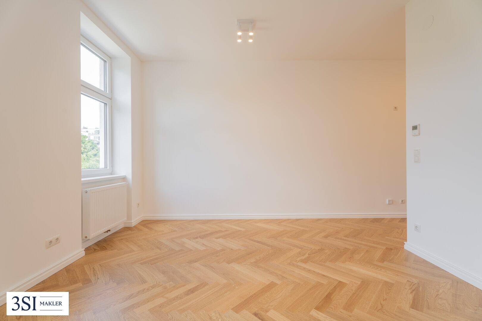Heller Raum mit Fischgrätparkett und einem Fenster, das viel Tageslicht hereinlässt.