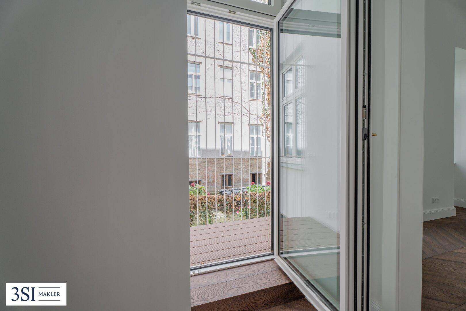 Kleiner Balkon mit Holzboden und Blick auf den begrünten Innenhof des Gebäudes.