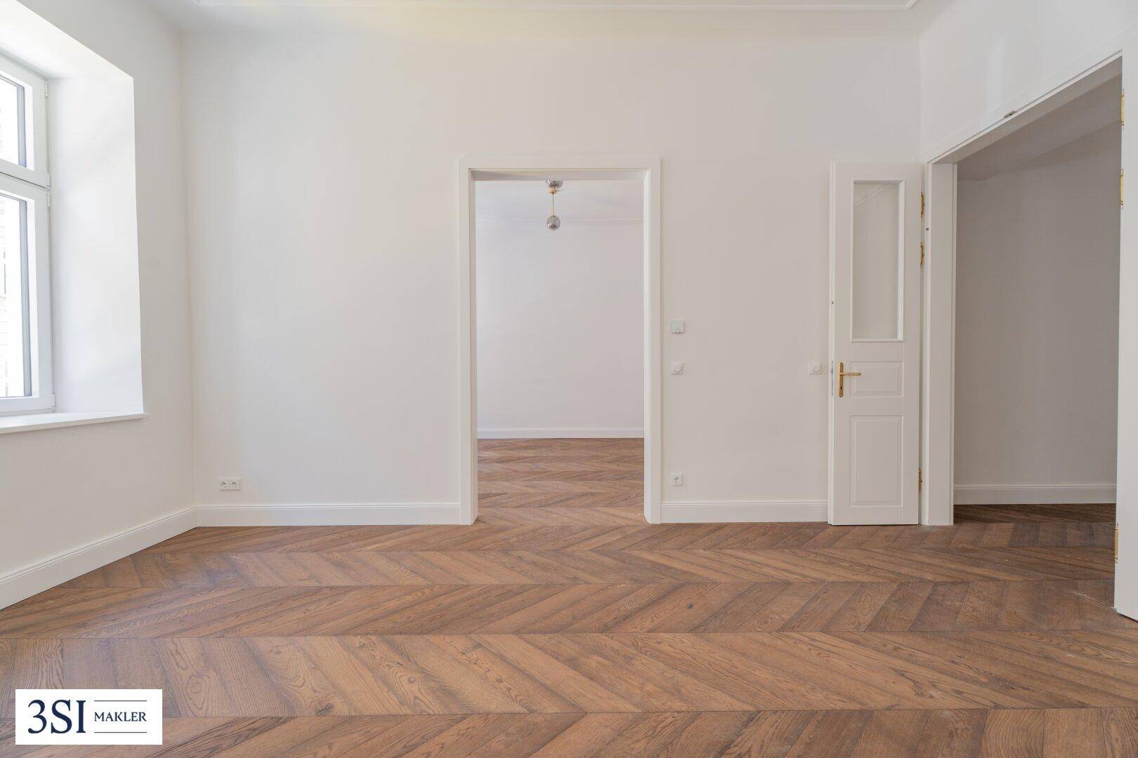 Geräumiges Zimmer mit Fischgrätparkett und hohen Decken, ideal für Wohn- oder Schlafbereich.