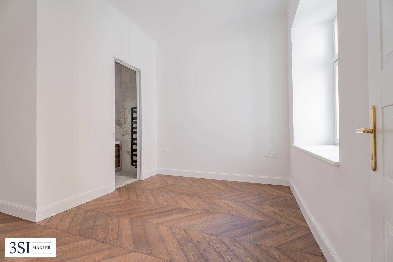 Helles Zimmer mit Fischgrätparkett und direktem Zugang zu einem modernen Badezimmer.
