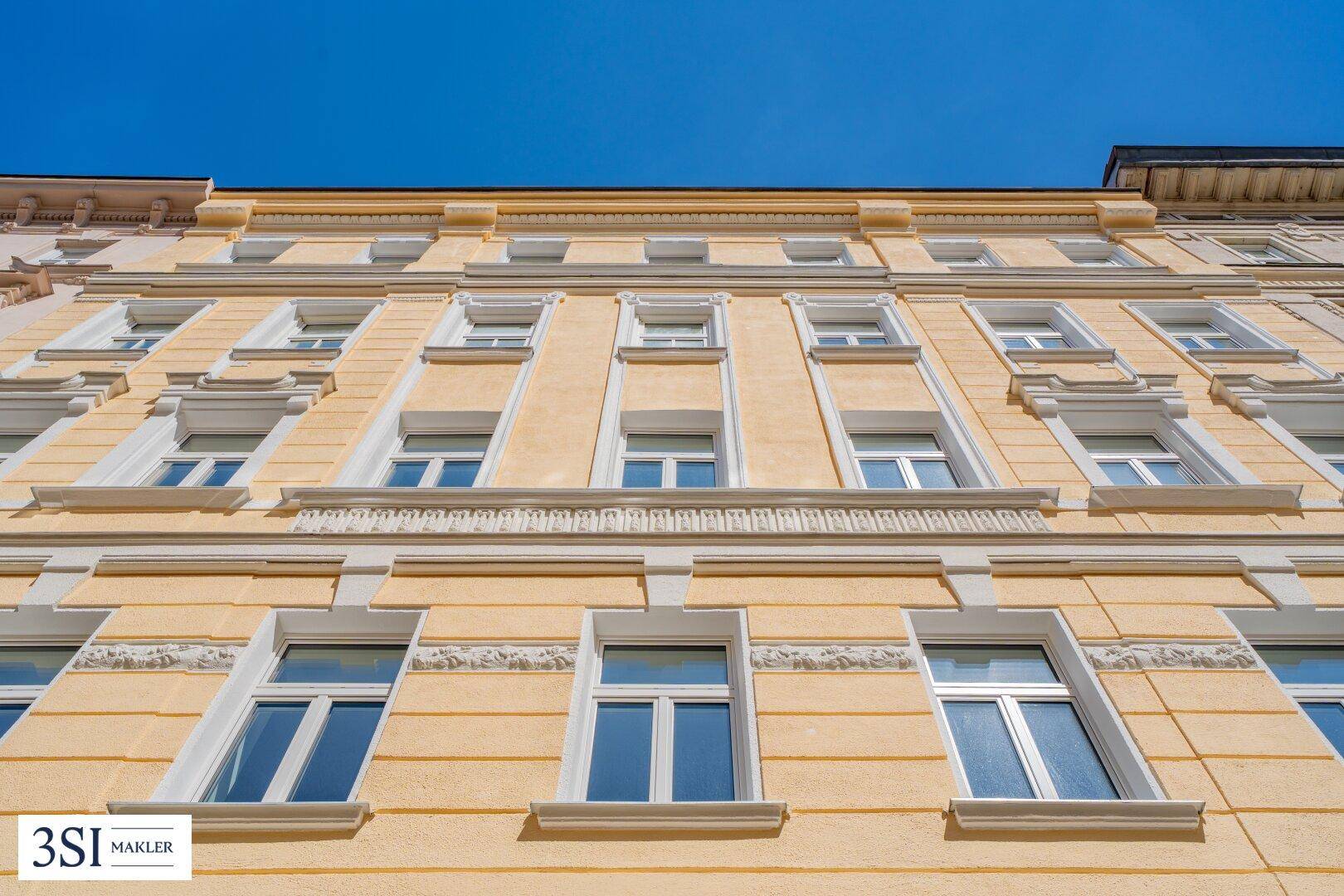 Detailansicht der historischen gelben Fassade mit ihren verzierten Fenstern unter blauem Himmel.