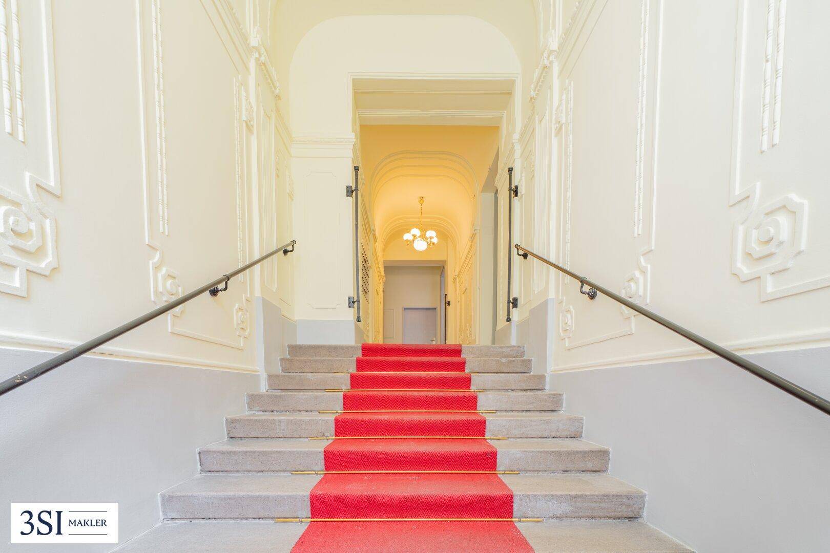 Repräsentatives Treppenhaus mit rotem Teppichläufer, verzierten Wänden und eleganten Handläufen.