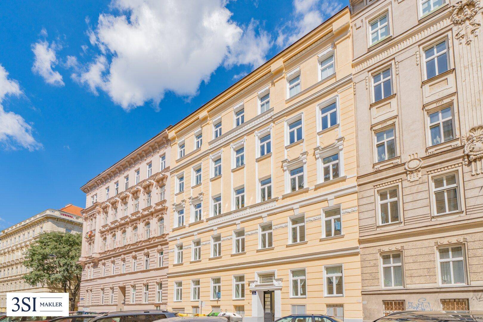 Ansicht der historischen gelben Gebäudefassade unter blauem Himmel mit angrenzenden Häusern.