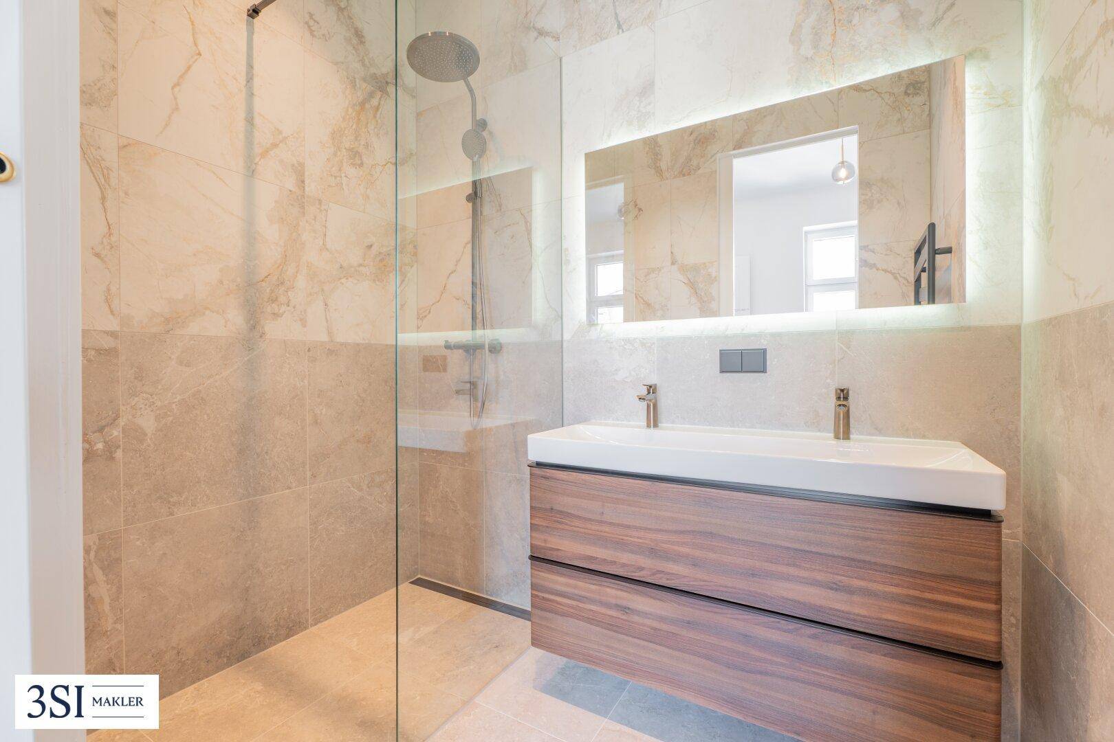 Modernes Badezimmer mit Waschtisch, beleuchtetem Spiegel und geräumiger begehbarer Dusche.