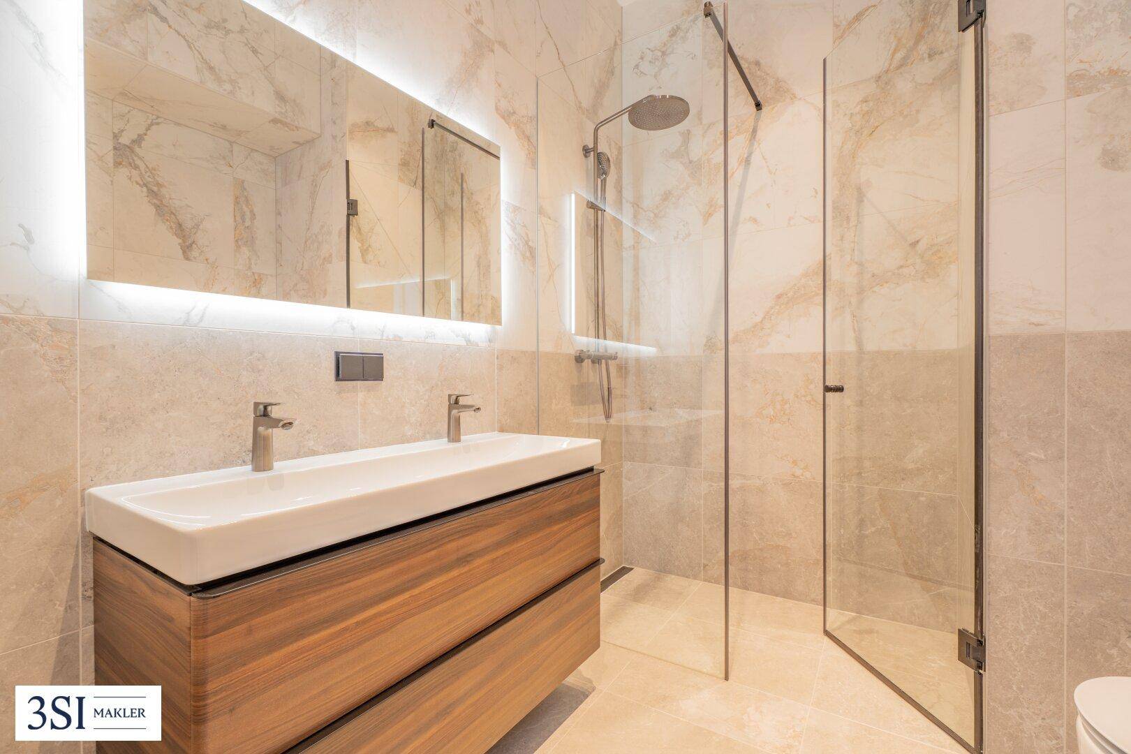 Modernes Badezimmer mit Doppelwaschbecken, beleuchtetem Spiegel und begehbarer Dusche.