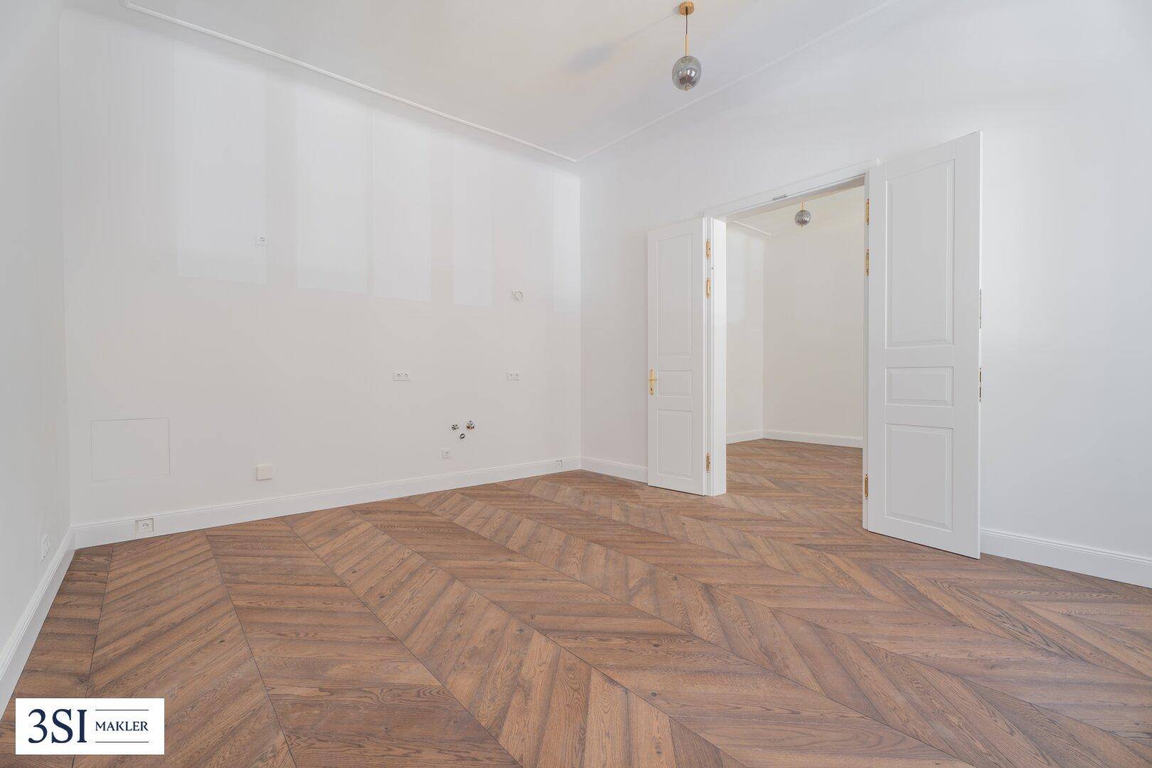 Leeres Zimmer mit Fischgrätparkett und weißen Wänden, bereit für die individuelle Gestaltung.