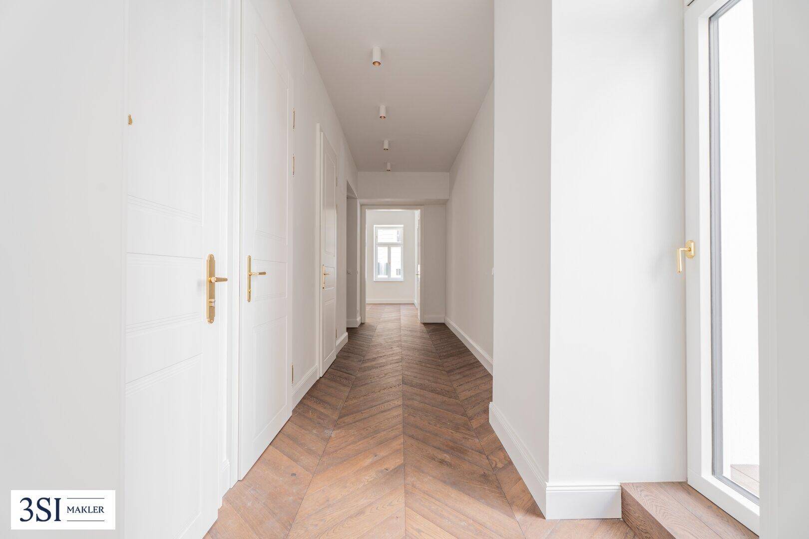 Heller Flur mit Fischgrätparkett und weißen Türen, der zu weiteren Räumen führt.