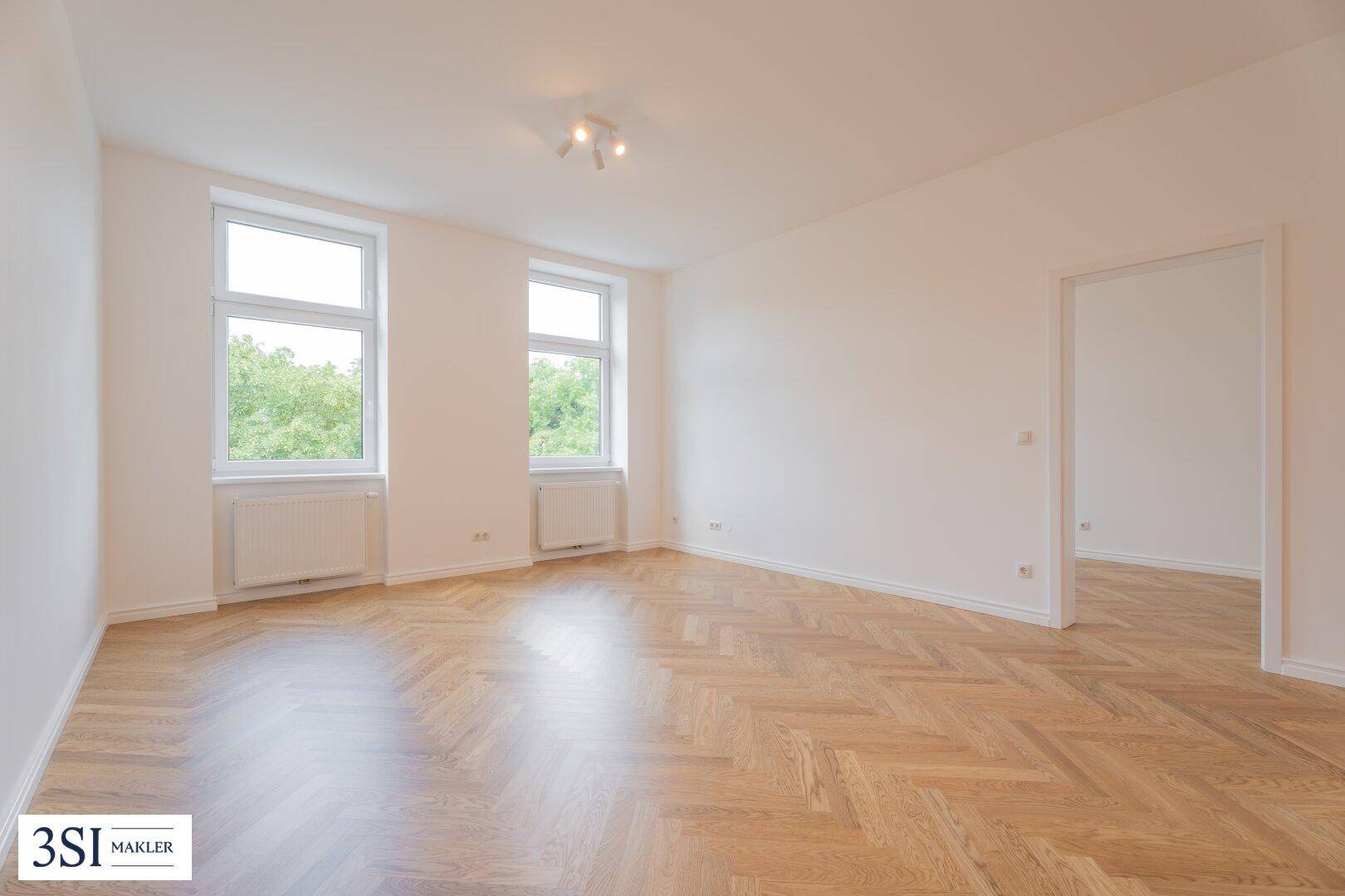 Geräumiges, leeres Zimmer mit Fischgrätparkett und großen Fenstern, bereit zur individuellen Gestaltung.