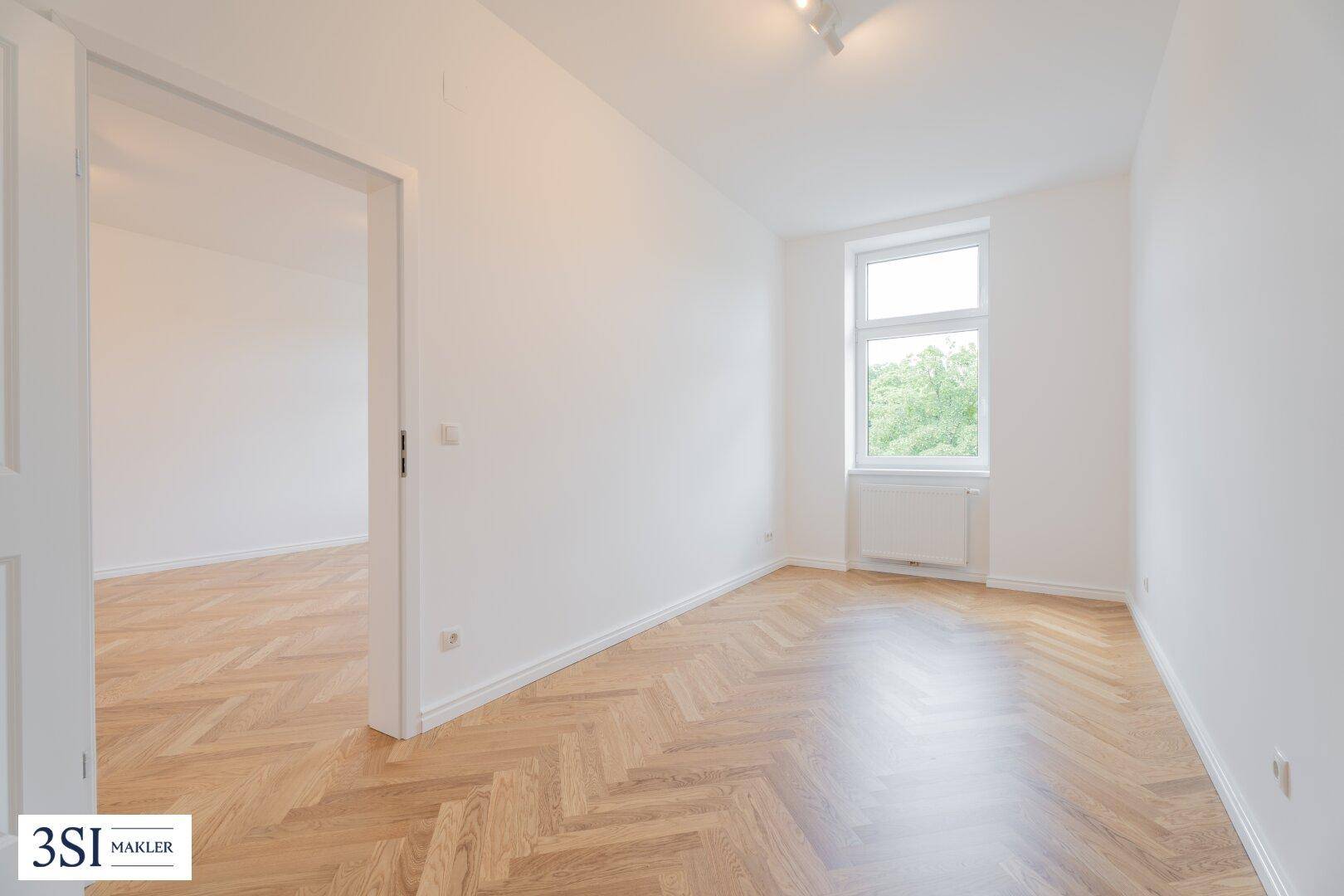 Kleiner, heller Raum mit Fischgrätparkett und einem Fenster, ideal als Schlaf- oder Arbeitszimmer.
