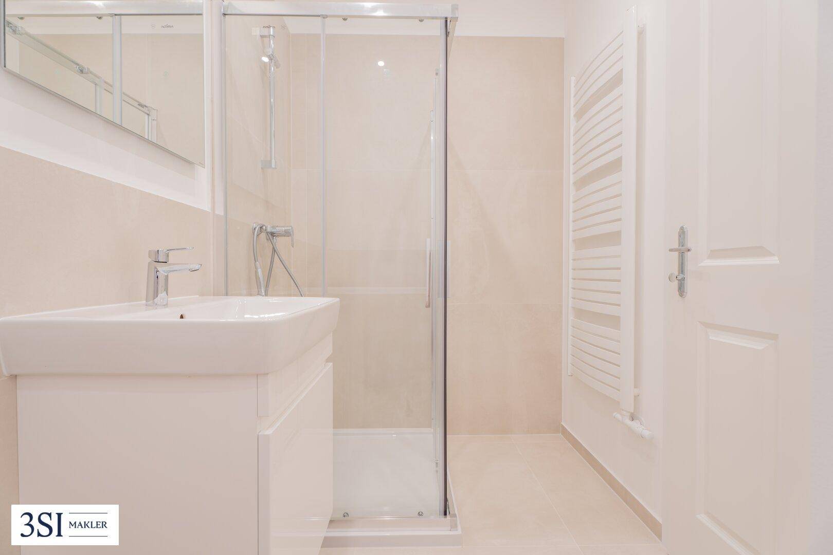 Helles Badezimmer mit moderner Duschkabine, Einzelwaschbecken und beheiztem Handtuchhalter.
